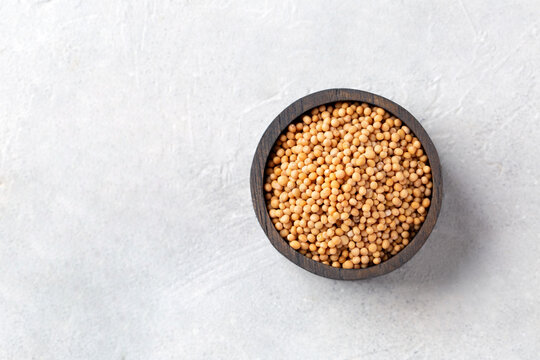 Mustard seeds in a wooden bowl on a light gray background. Top view.
