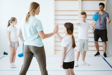 Girl doing high five with her teacher during physical education at school - Powered by Adobe