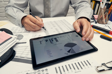 Business analysis and accounting concept - businessman working with document, spreadsheet, using calculator, tablet pc. Office desk closeup.