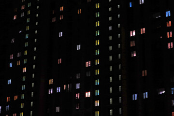 Fototapeta na wymiar Luminous windows in an apartment building at night, where each tenant has his own apartment