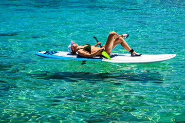 Woman is lying on a SUP with some graffition, crystal clear waters and sunbathing on a hot sunny day. Healthy lifestyle concept.