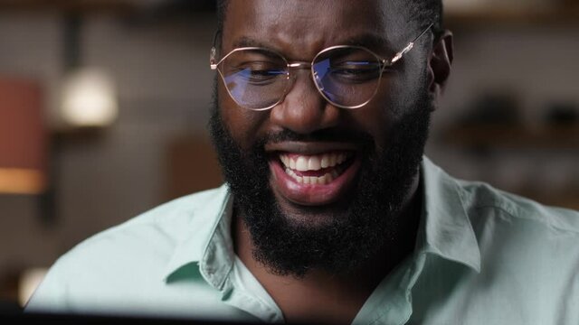 Joyful dark-skinned man looking at computer screen, advertisement of black Friday reflected in his glasses. Excited african american male shopping in online stores during black Friday discounts