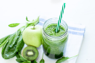 Healthy green smoothie with spinach in a mug with a strip of linen cloth on a white table background