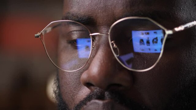 Face of african american man in glasses during online shopping on laptop. Dark-skinned male scrolling web pages while choosing clothes in online store, close-up of pc screen reflected in his glasses