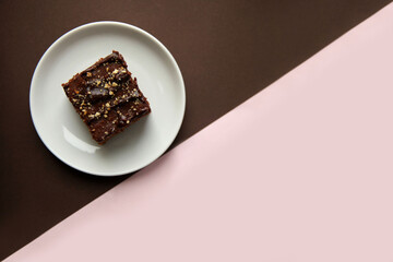A chocolate piece of cake with nut crumbs on a brown and pink geometric background.
