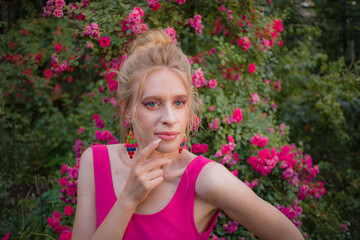 blonde with curly hair and beautiful makeup in a dress on a background of blooming roses