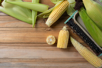 Green corn arranged on a wooden table and a scale. Top view.