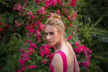 Naklejka premium blonde with curly hair and beautiful makeup in a dress on a background of blooming roses