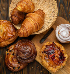 Assorted pastries, croissants, buns. On a brown wooden table.
