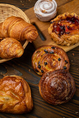 Assorted pastries, croissants, buns. On a brown wooden table.
