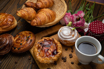 Assorted pastries, croissants, buns. On a brown wooden table.
