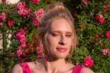 Fototapeta premium blonde with curly hair and beautiful makeup in a dress on a background of blooming roses