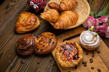 Assorted pastries, croissants, buns. On a brown wooden table.
