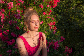 Naklejka premium blonde with curly hair and beautiful makeup in a dress on a background of blooming roses
