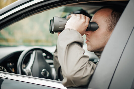 A young hunter is sitting in the car and looks into the binoculars. He is trying to find some wild animals.