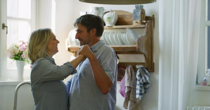 Authentic shot of lovely happy mature couple is enjoying time together and having fun dancing to celebrate their timeless love in a kitchen at home. Concept: love, family, marriage, home