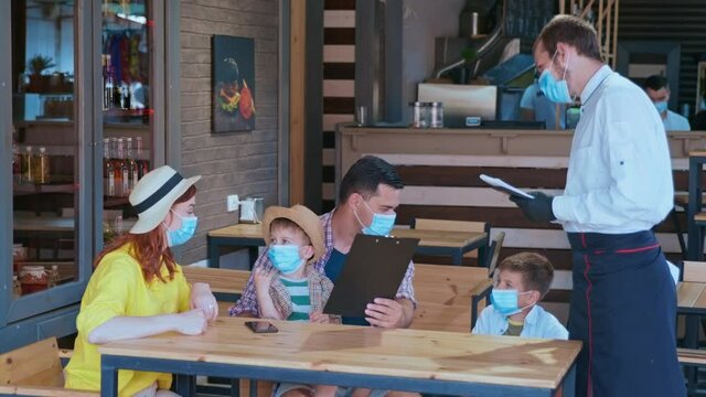small business quarantine, happy visitors friendly family with children in medical masks for virus and infection protection order waiter in medical gloves and mask food and drinks from restaurant menu