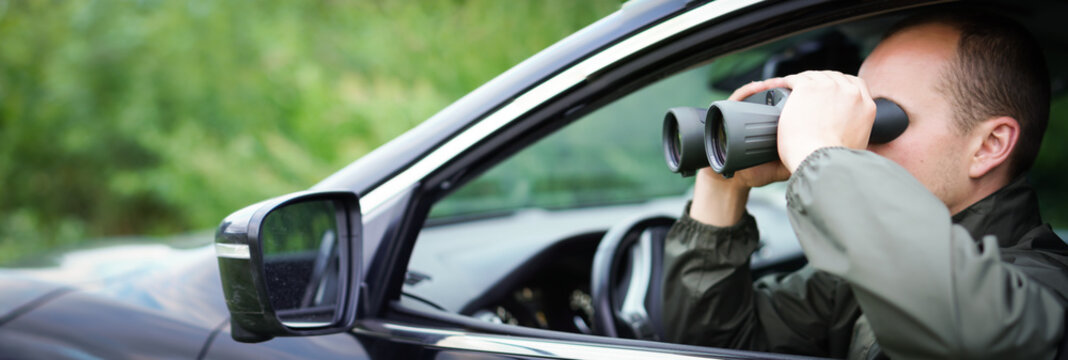 Panorama a young hunter is sitting in the car and looks into the binoculars. He is trying to find some wild animals.