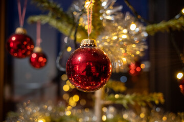 red shiny christmas balls hang from a festively decorated christmas tree