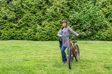 Naklejka premium pregnant woman on the green lawn in a park holding bicycle ready to ride.