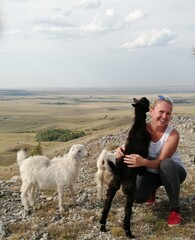 A young wooman on top of a hill with white and black goats