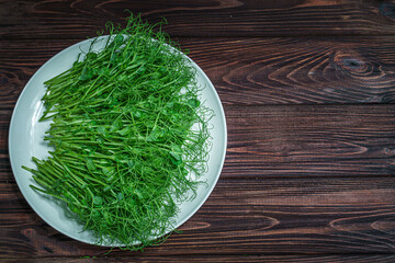 Top view of fresh cutted pea microgreen sprouts on plate on wooden surface/