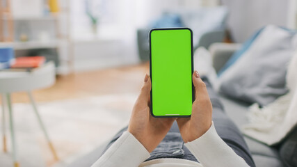 Young Woman at Home Lying on a Couch using with Green Mock-up Screen Smartphone. Girl Using Mobile...