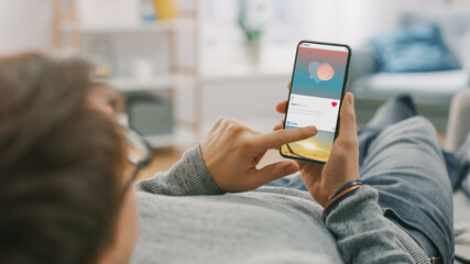 Man at Home Lying on a Couch using Smartphone, Scrolling Social Media Feed, Checking News, Friends...
