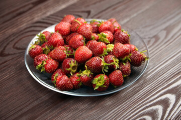 Strawberries on a glass plate on wooden background. Red ripe berries, fresh juicy strawberries