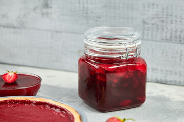 Jar with homemade strawberry jam on grey wooden background