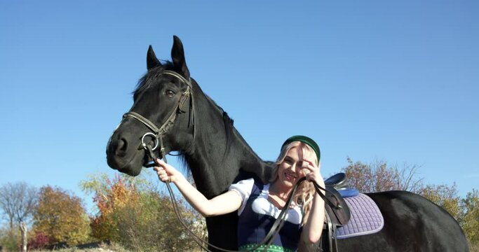 Happy Slavic girl poses with black horse at camera among the wide meadows