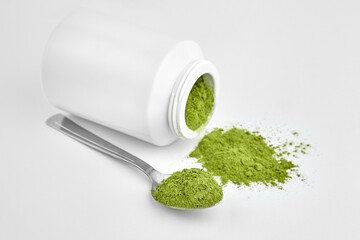 Freeze dried young organic wheatgrass powder in teaspoon and jar on white.