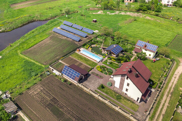 Aerial view of a private house in summer with blue solar photo voltaic panels on roof top and in the yard.
