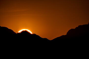 Alba in montagna con sole che sorge seminascosto dalle cime 