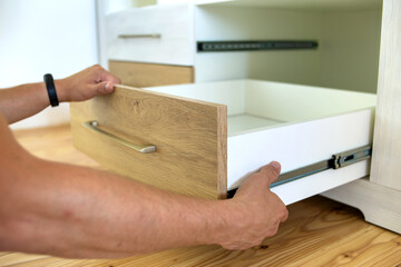 Close up of carpenter hands installing wooden drawer on sliding skids in contemporary cupboard...
