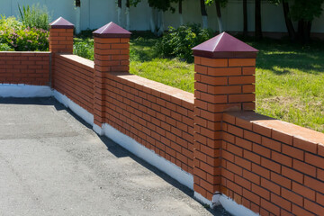 decorative brick fence with turrets separates the asphalt from the green lawn © Vitaliy