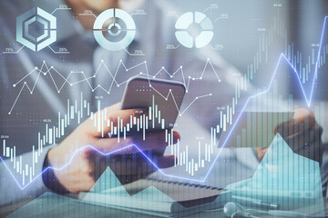 Double exposure of man's hands holding and using a phone and financial graph drawing. Analysis concept.