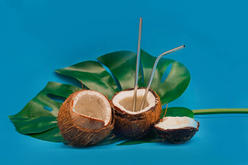 Coconut halves with reusable drinking straws on monstera leaf. Minimalistic summer concept