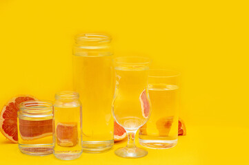 Grapefruit distorted through glasses with water. Summer concept. Yellow background