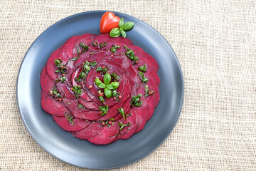 Fresh beetroot carpaccio with basil leaf, heart shaped cherry tomato.