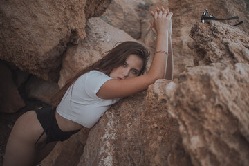 young brunette with long hair in a white top and black swimsuit on a background of rocks
