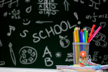 School background with stationery accessories. Books, globe, pencils and various office supplies lying on the desk on a green blackboard background