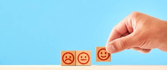 concept of satisfaction or service rating. man arranges wooden blocks with a displeased and contented smiley