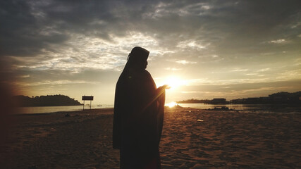 Fototapeta premium A muslim woman on the beach before sunset