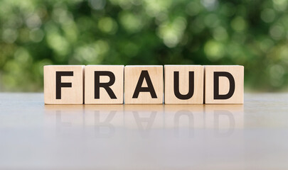 FRAUD word written on wooden blocks. The text is written in black letters and is reflected in the mirror surface of the table.
