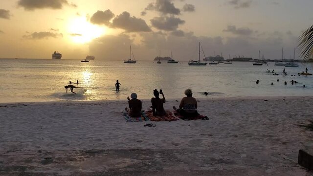 Black people sitting talking enjoying sunset at the beach in beautiful Barbados, Caribbean. Island scenes and silhouettes on phone