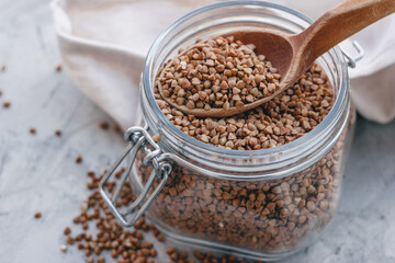 buckwheat in a glass jar with a wooden spoon, on a gray light background. Space for text, copy space