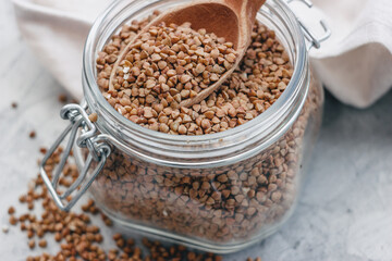 buckwheat in a glass jar with a wooden spoon, on a gray light background. Space for text, copy space