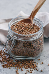 buckwheat in a glass jar with a wooden spoon, on a gray light background. Space for text, copy space
