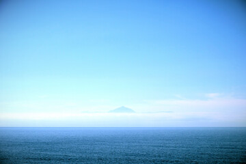 Seascape with a distant view of a volcanic cone visible through sea mist above the horizon. Slight vignette added.